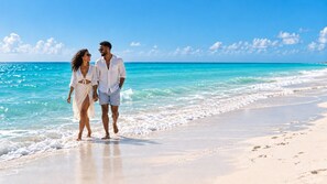 A couple walking on a sandy beach with clear blue water and a clear sky. - Ellipse Resort, Grace Bay /Jr Suite One Bedroom with Grace Bay Street View (Grace Bay)