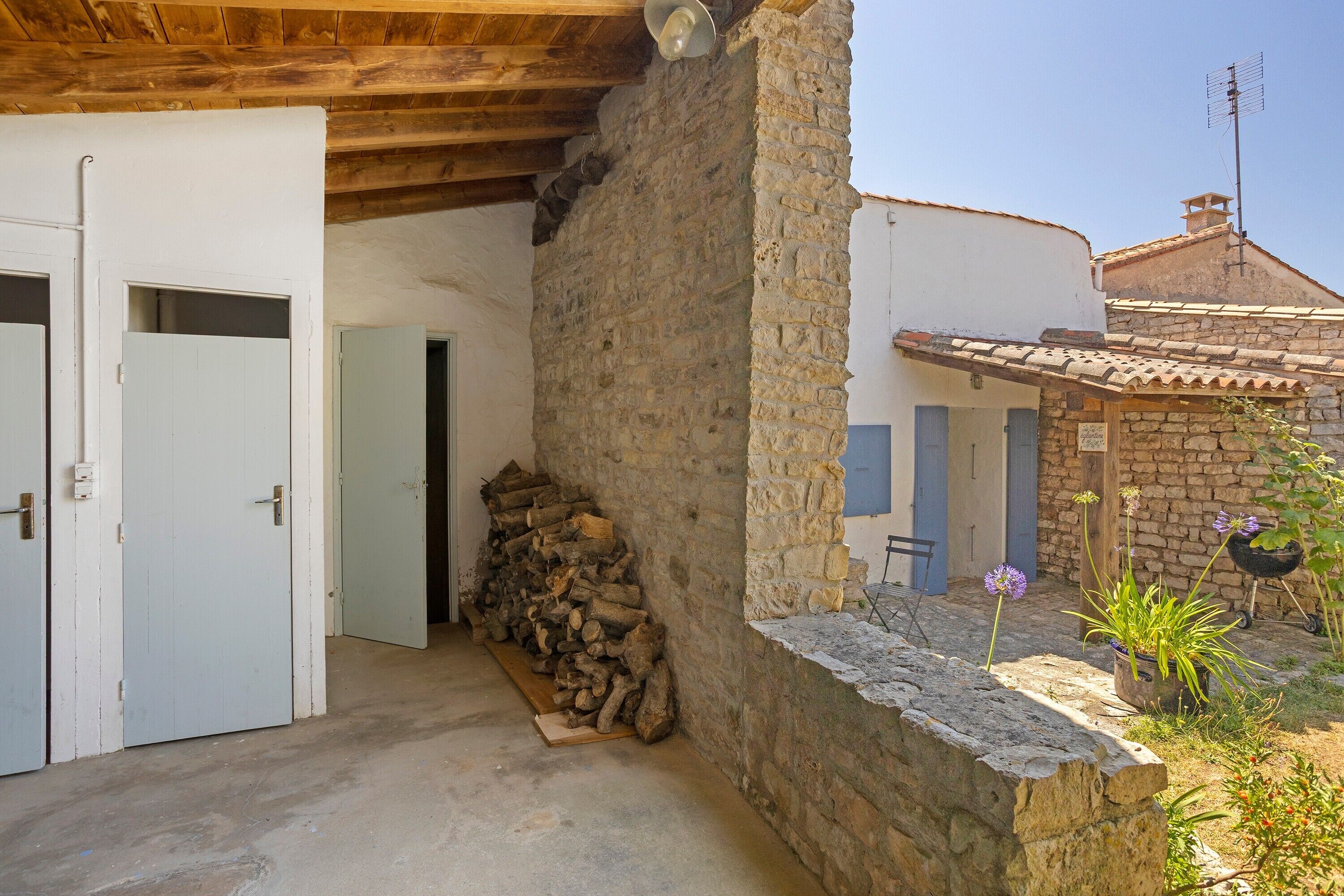Un bâtiment rustique avec un mur en pierre, une porte en bois et une pile de bois de chauffage.