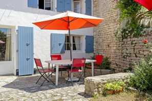 A patio with a table and chairs, a red umbrella, and a stone wall. - “Maison De Pays Églantine” with Private Terrace, Garden, and Wi-Fi (Sainte-Marie-de-Ré)