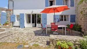 A two-story building with a stone facade, a tiled roof, and a patio area with a table and chairs. - “Maison De Pays Églantine” with Private Terrace, Garden, and Wi-Fi (Sainte-Marie-de-Ré)