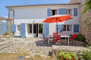 A two-story building with a stone facade, a tiled roof, and a patio area with a table and chairs. - “Maison De Pays Églantine” with Private Terrace, Garden, and Wi-Fi (Sainte-Marie-de-Ré)