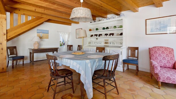 A dining area with a table set for four, surrounded by chairs, under a wooden ceiling with exposed beams. - “Maison De Pays Églantine” with Private Terrace, Garden, and Wi-Fi (Sainte-Marie-de-Ré)
