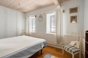 A bedroom with a bed, a chair, a window with curtains, and a wall-mounted mirror. - “Maison De Pays Églantine” with Private Terrace, Garden, and Wi-Fi (Sainte-Marie-de-Ré)