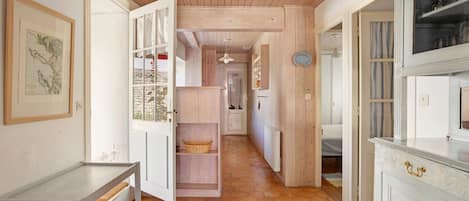 A hallway with wooden flooring, open doors leading to different rooms, and a hanging light fixture.