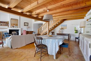 A spacious room with a wooden ceiling, a dining table with chairs, a fireplace, and a staircase. - “Maison De Pays Églantine” with Private Terrace, Garden, and Wi-Fi (Sainte-Marie-de-Ré)