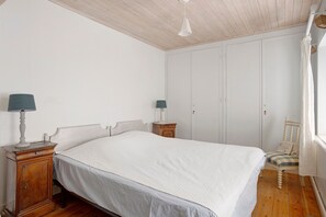 A bedroom with a large bed, two bedside tables, a wardrobe, and a chair. - “Maison De Pays Églantine” with Private Terrace, Garden, and Wi-Fi (Sainte-Marie-de-Ré)