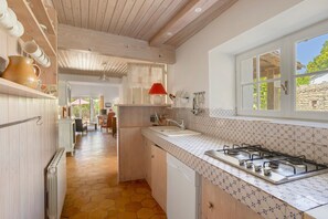 A kitchen with a gas stove, a sink, and a window overlooking a garden. - “Maison De Pays Églantine” with Private Terrace, Garden, and Wi-Fi (Sainte-Marie-de-Ré)