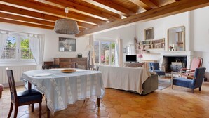 A spacious living room with a high wooden ceiling, a dining area with a table set for two, and a fireplace with bookshelves. - “Maison De Pays Églantine” with Private Terrace, Garden, and Wi-Fi (Sainte-Marie-de-Ré)