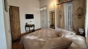 Une chambre à coucher avec un grand lit, un téléviseur fixé au mur, une porte en bois et une fenêtre avec des rideaux.