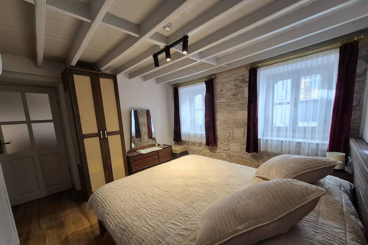 Quarto com cama, cômoda, espelho e janela com cortinas.