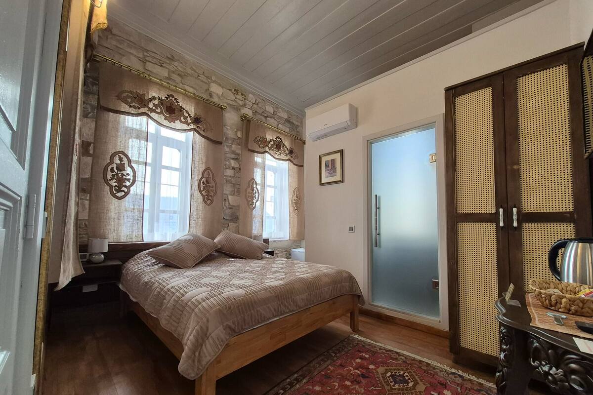 Quarto com cama de madeira, parede de pedra e porta com painel de tecido.