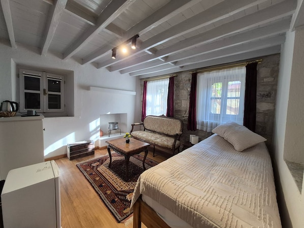 Una habitación con cama, sofá, una mesita, un radiador y una ventana con cortinas.