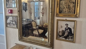 Une pièce comprenant un grand miroir décoratif, plusieurs photographies encadrées, une table en bois et une chaise.