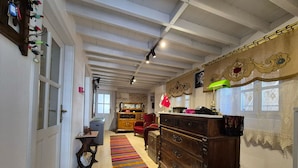 Une pièce spacieuse avec un plafond haut, une commode en bois, un fauteuil rouge, une petite table et un tapis rayé aux couleurs vives.