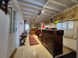 Una habitación amplia con techo alto, un aparador de madera, una silla roja, una mesita pequeña y un tapete colorido a rayas.
