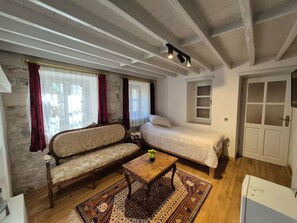 Una habitación con sofá, cama, una mesita con una planta, ventana con cortinas y una puerta.