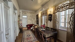 Une pièce avec un plancher en bois, une table à manger avec des chaises, un canapé rouge, un tapis à motifs et un mur en pierre.