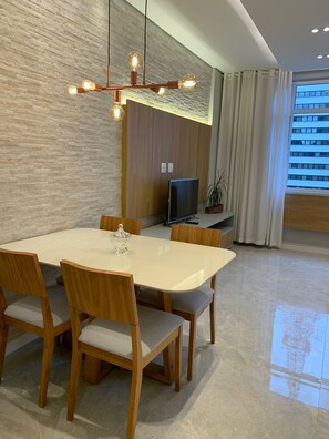 Ein modernes Wohnzimmer mit Essbereich, einem Flachbildfernseher und einem großen Fenster mit Vorhängen.