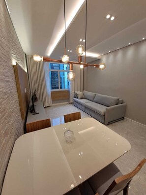 Ein modernes Wohnzimmer mit einem weißen Esstisch, einem grauen Sofa und einer außergewöhnlichen Deckenleuchte.