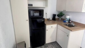 Une cuisine compacte équipée d’un four à micro-ondes, d’un réfrigérateur, d’un évier et d’un petit plan de travail.