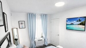Une chambre avec un lit, une fenêtre avec des rideaux, un téléviseur fixé au mur et une porte.