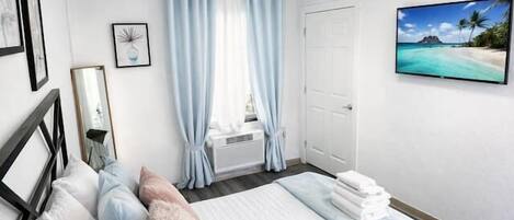 A bedroom with a bed, a window with curtains, a TV on the wall, and a door.