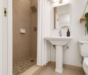 Ein Badezimmer mit Dusche, Waschbecken, Toilette und einem Spiegel mit einem dekorativen Gegenstand darüber.