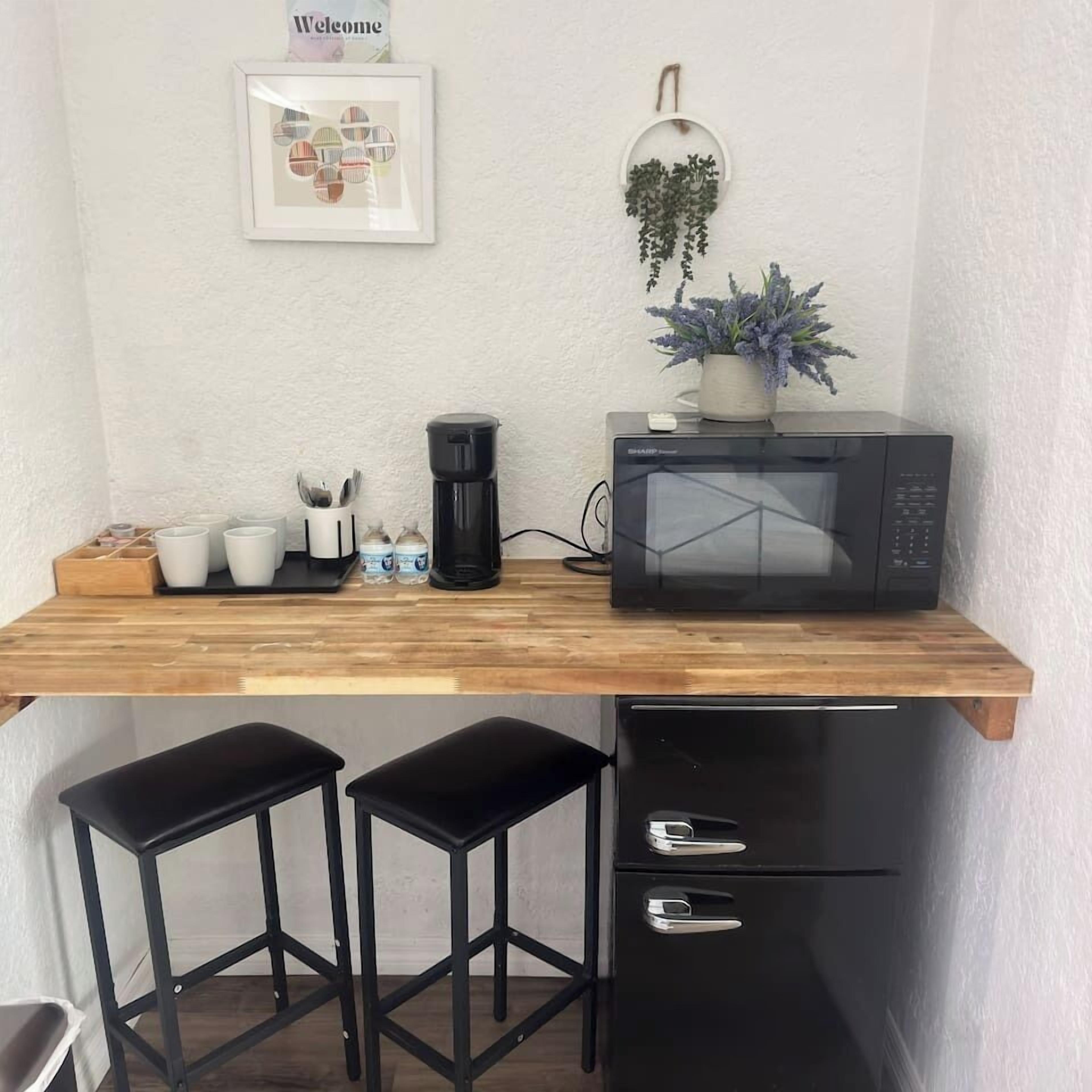 Una cocina pequeña equipada con microondas, cafetera y dos taburetes de bar.