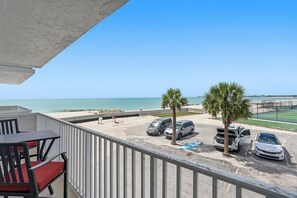 Ein Balkon mit Blick auf den Strand, parkende Autos und eine Palme.