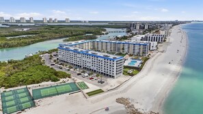 Ein Strandhotel mit mehreren Gebäuden, einem Strand und einem Tennisplatz.