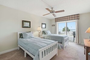 Ein Schlafzimmer mit zwei Betten, einem Deckenventilator, einem Fenster mit Blick und einem Balkon.