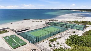 A tennis court complex with multiple courts, a sandy beach, and a view of the ocean. - Your Front-Row Seat to Gulf Sunsets on Bonita Beach (Bonita Springs)