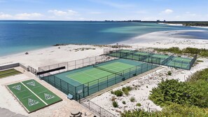 Ett tenniscenter med flera banor, en sandstrand och utsikt över havet.
