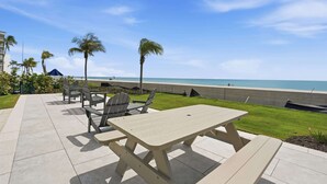 A patio with outdoor furniture, a view of the ocean, and palm trees. - Your Front-Row Seat to Gulf Sunsets on Bonita Beach (Bonita Springs)
