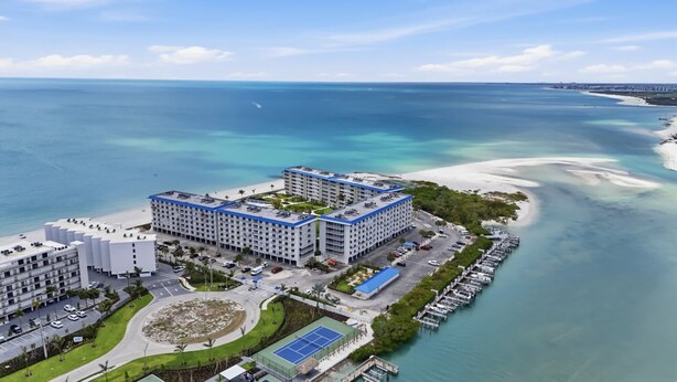 A coastal hotel with multiple buildings, a parking lot, a tennis court, and a marina. - Your Front-Row Seat to Gulf Sunsets on Bonita Beach (Bonita Springs)