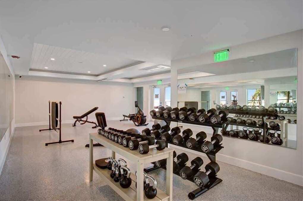 Un gimnasio con equipo de levantamiento de pesas, una banca y un espejo que refleja la sala.