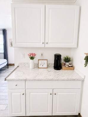 A kitchen with white cabinets, a marble countertop, a coffee maker, a small plant, and a framed sign. - Clearwater Getaway w/ Pool • 3 Miles to Beach #4 (Clearwater)