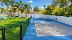 A tennis court with a net, surrounded by a white fence and palm trees. - Clearwater Getaway w/ Pool • 3 Miles to Beach #4 (Clearwater)
