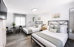 Ein Hotelzimmer mit zwei Betten, einem Schreibtisch, Stühlen, einer Topfpflanze und Bildern an den Wänden.