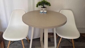 Mesa redonda com duas cadeiras brancas, uma pequena planta em vaso e uma garrafa de água.