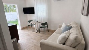 A modern living room with a sofa, a small round table with a plant, a TV mounted on the wall, and a dining area with chairs. - Studio 3 miles from the Beach, with pool #512 (Belleair)