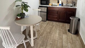 A compact kitchen with wooden cabinets, a microwave, a sink, and a small dining table with chairs. - Cozy apartment with pool in Clearwater #515 (Belleair)