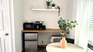 Cocina compacta con refrigerador, microondas, cafetera y un pequeño estante con plantas y tazas.