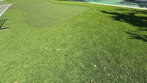 Un patio trasero con césped artificial, una valla blanca y árboles.