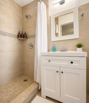Une salle de bain avec une douche, un lavabo avec un miroir et une petite étagère contenant des articles de toilette.