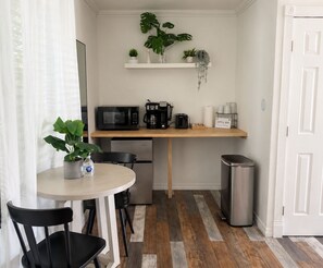 A compact kitchenette with a microwave, coffee maker, and a small refrigerator. There is a table with chairs and a potted plant. - King Suite w Pool, 3 Miles from Clearwater Beach#7 (Clearwater)