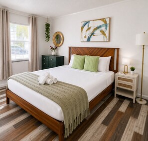 A neatly made bed with a wooden headboard, a bedside table with a lamp, and a wall-mounted abstract painting. - King Suite w Pool, 3 Miles from Clearwater Beach#7 (Clearwater)