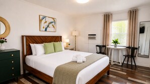 Una habitación de hotel con una cama de madera, un escritorio, una silla, una lámpara y un cuadro en la pared.