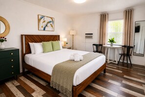 A hotel room with a wooden bed, a desk, a chair, a lamp, and a painting on the wall. - King Suite w Pool, 3 Miles from Clearwater Beach#7 (Clearwater)