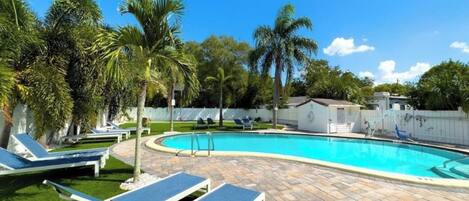 A swimming pool with lounge chairs, palm trees, and a clear blue sky.